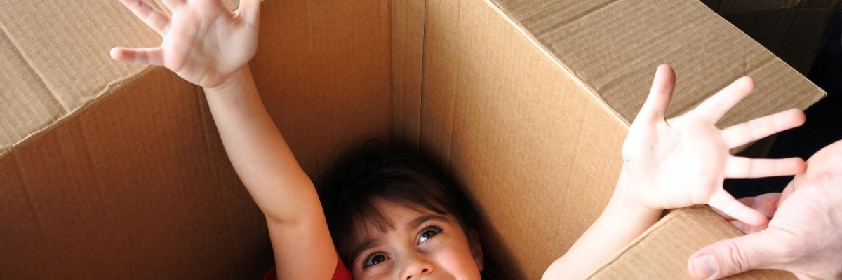 Happy girl (age 6-7) inside a big cardboard box moving into a new house. Moving home concept. Real people. copy space